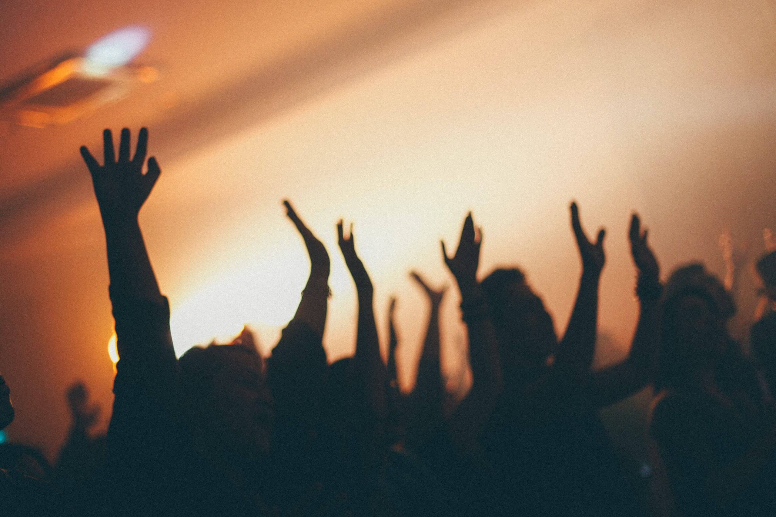 Audience raising their hands, silhouetted against warm light